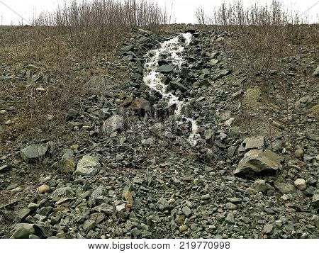 Waterfall from the thawed waters. Melting snow in the hilly tundra. Waterfall