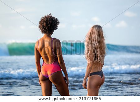 surfer girls in bikini watching surfer riding waves at beautiful Padang Padang beach, Bali, Indonesia