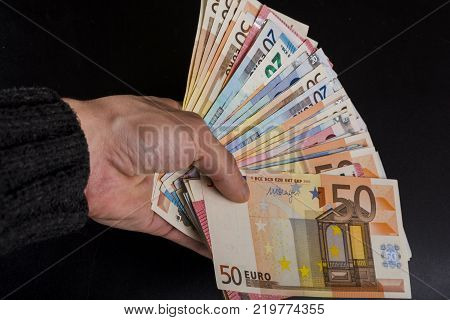 Human hand holding money - fifty-twenty-ten euro banknotes isolated on a dark gray background