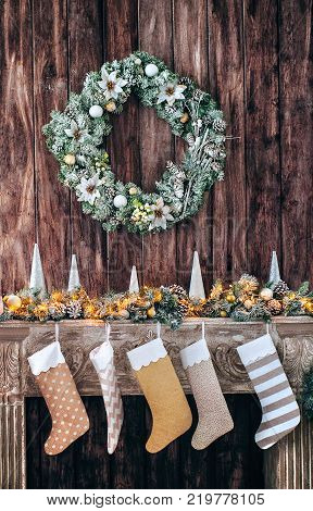 Christmas socks on decorated fireplace, background of a wooden wall with a green wreath.