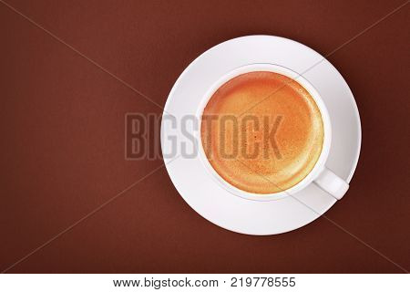 Close up white cup full of espresso coffee with crema froth on porcelain saucer over brown paper background close up elevated top view directly above