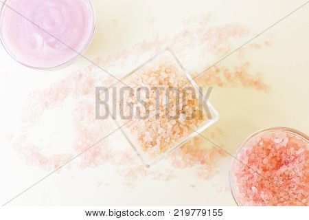 Spa and bodycare concept. Tree glass clear bowls with rose and peach bath salt and pink face or body mask, salt grains scatted on the table, top view. Space for a text or product display.