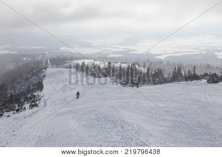 Snow-covered ski slopes against the backdrop of mountain valley on a foggy winter day. People skiing. Strbske Pleso High Tatras Slovakia. Concept of a healthy sport lifestyle. Destination of the winter holidays.