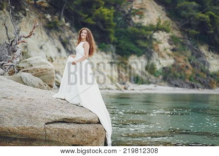 Beautiful long-haired bride in a magnificent white dress walking near water