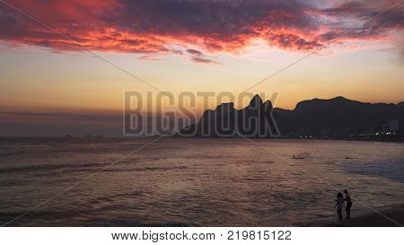 Wide picture of a red sunset in Arpoador with a single couple at the beach. Rio de Janeiro Brazil.