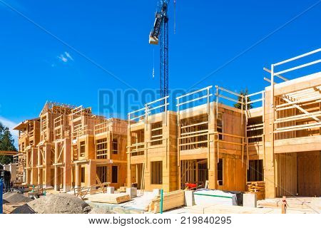 New residential building under construction with the crane about. Low rise wooden framework of the building on concrete base