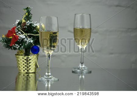 Two glasses of champagne among the fir branches on a dark background. One glass with foam and a glare of reflected light second glass with yellow sparkling wine. The inscription of a happy new year.
