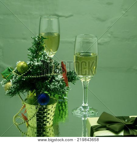 Two crystal glasses with soda on a black background with spruce branches. A stream of carbonated liquid pours into the glass.