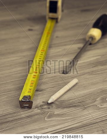 Closeup of measure tape screwdriver and pencil on a wooden background