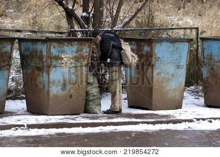 Homeless old man in search for food. Poor tramp hungry rummaging for some food in garbage.