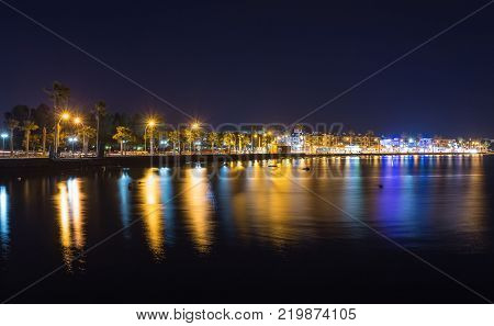 View over the seafront of the city Paphos in Cyrpus. Palm silhouettes, boats in the water and golden sunset over the sea with dramatic cloudy sky.