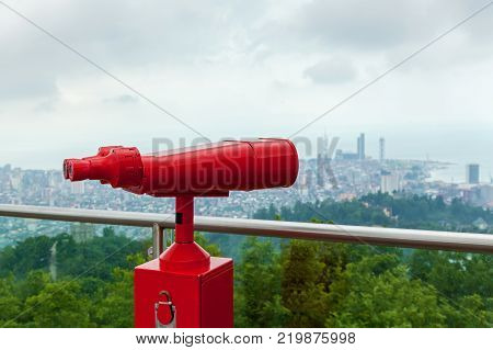 Coin operated red binocular towerview on observation deck with view on the sea and city