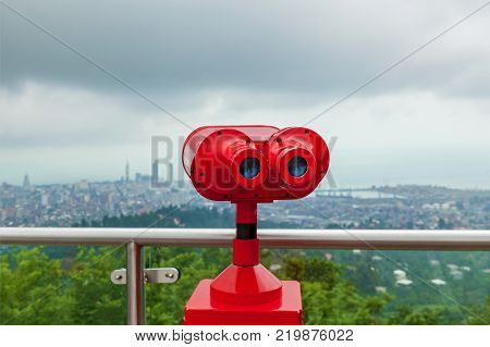Coin operated red binocular towerview on observation deck with view on the sea and city
