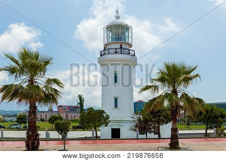 Lighthouse against the background of the city. A white lighthouse against a light blue sky in day light.