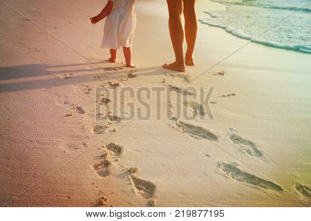 mother and little daughter walking on beach leaving footprint in sand