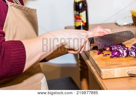 Female hands chopping red cabbage with knife on wooden board.