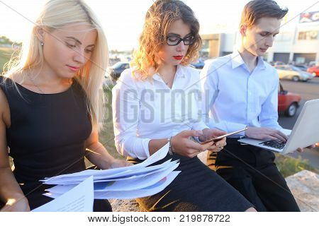 Young contemporary confident people, two boys and two girls, perspective entrepreneurs, students smiling, chatting with each other, using gadgets, laptops, tablet and smartphone for work with office programs, drawing up business plan, discuss working mome