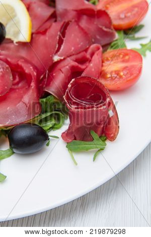 a white dish of bresaola and aragula
