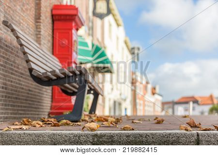 autumn leaves on the pavement, bench and red mailbox in the background
