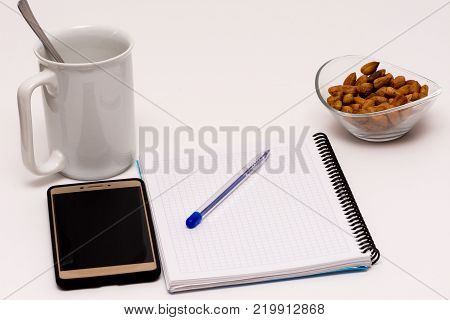 mobile phone and notebook on the desk with bowl of huzelnuts and the cup of coffee for keeping energy while working