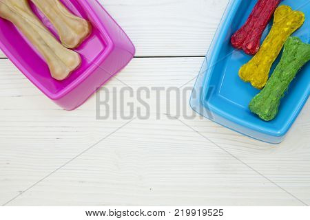 Pet care, veterinary concept. Training and feeding a dog. A pink plastic bowl with chewing dog bones and a blue bowl with colorful chrunchy bones.White wooden background. space for atext or image