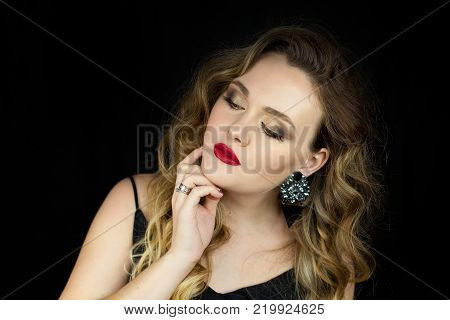 Portrait of a young beautiful woman with red lipstick on a black background. Makeup. Holidays.