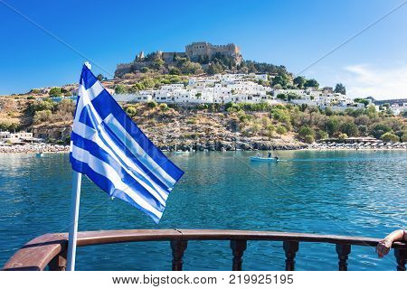Bay of Lindos, Grrek flag and acropolis of Lindos in background (Rhodes, Greece)