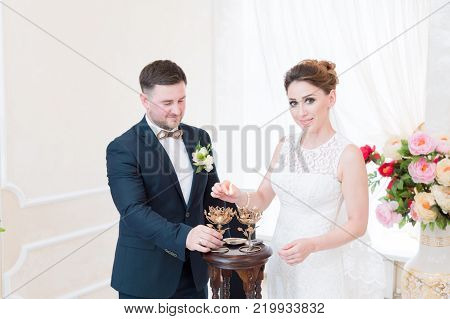 A beautiful happy couple in the registry office performs a wedding ritual with candle lighting. The concept of a happy marriage and marriage procession in the registry office.