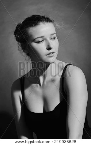 A pretty young female is posing in a photo studio. She is wearing a black crop top. With exposed shoulders. She has nice brown hair.  On a grey background. Shee is looking to the side.