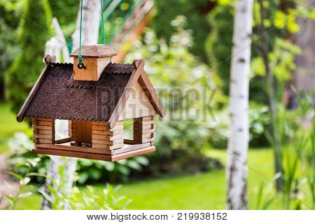 A feeder for birds made in a form of a house in a garden.