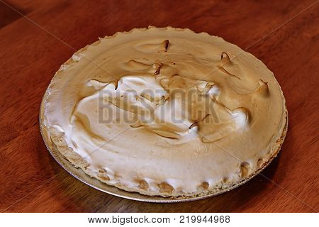 Lemon meringue pie on cutting board on brown wooden background
