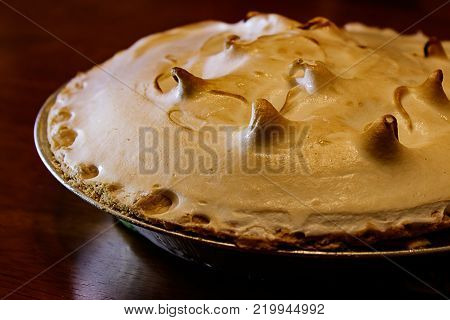 Lemon meringue pie on cutting board on brown wooden background