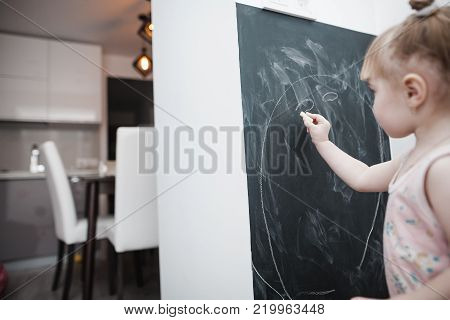 Cute little girl drawing on blackboard. Toddler girl having fun outdoors, holding chalk and drawing.