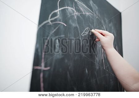 Cute little girl drawing on blackboard. Toddler girl having fun outdoors, holding chalk and drawing.