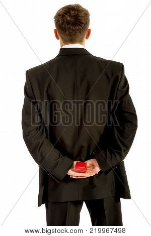 18 year old wearing a tuxedo hiding a ring box behind his back isolated on a white background