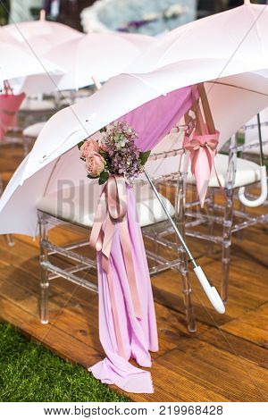 Chairs, flowers and umbrellas at an outdoor ceremony.