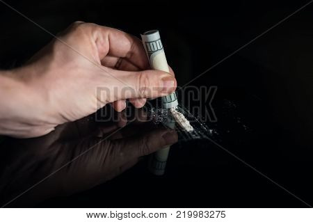 Man hands rolls dollar banknote for using cocaine powder lines, Drug addiction concept. A line of coke with a hundred dollar bill on black background. concept of addiction