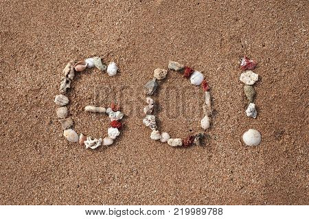 Text Go on sandy beach made from shells. Concept of travel and active lifestyle