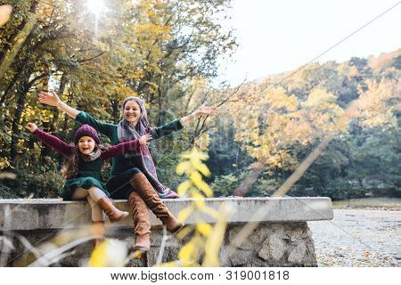 A Mother With A Toddler Daughter Sitting In Forest In Autumn Nature, Stretching Arms.