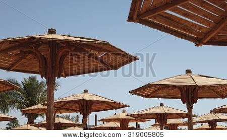 Hats Of Wooden Beach Umbrellas Against The Blue Sunny Sky In Summer