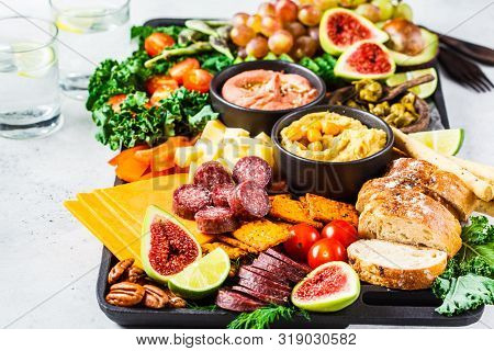 Meat And Cheese Appetizer Platter. Sausage, Cheese, Hummus, Vegetables, Fruits And Bread On A Black 