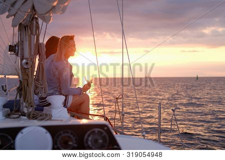 Two Joyful Women Are Celebraiting Good Summer Day At The Yacht While Watching Beautiful Sunset.