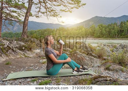 Blond Beautiful Girl Sitting On The Mat On The Stone Ground Drinking Coffee Or Tea, Resting After Sp