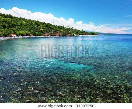 Trooppisen laguunin kirkas vesi ja rakennukset metsän rinteellä. Amed kylä, Indonesia