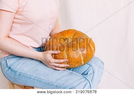 Woman In Blue Jeans And Pink T-shirt Holding A Big Pumpkin