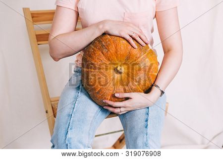 Woman In Blue Jeans And Pink T-shirt Holding A Big Pumpkin