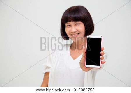 Portrait Of Asian Senior Wowan Showing Or Presenting Mobile Phone Application On Hand Isolated Over 