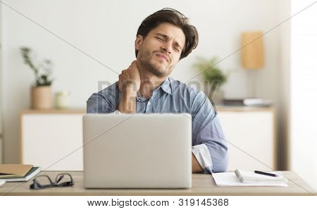 Neck Pain. Man Having Bad Neckache Working On Laptop At Workplace.