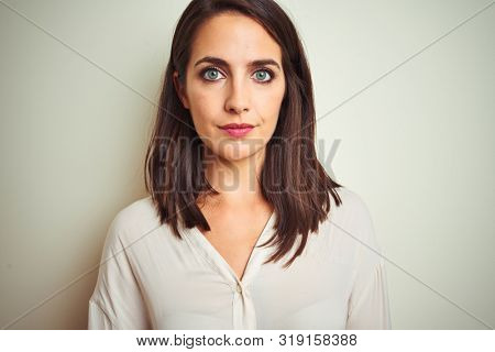 Young beautiful woman wearing casual shirt standing over white isolated background with serious expression on face. Simple and natural looking at the camera.