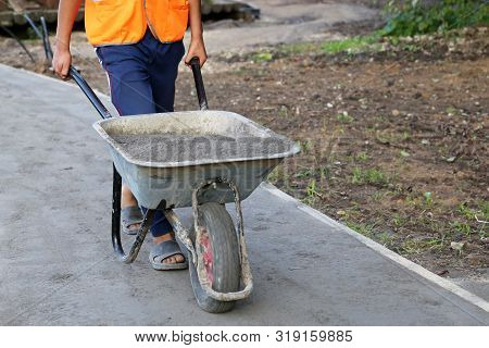 Worker Carries A Wheelbarrow With The Ground. Man With Cargo, Concept Of Earthworks, Digging, Constr